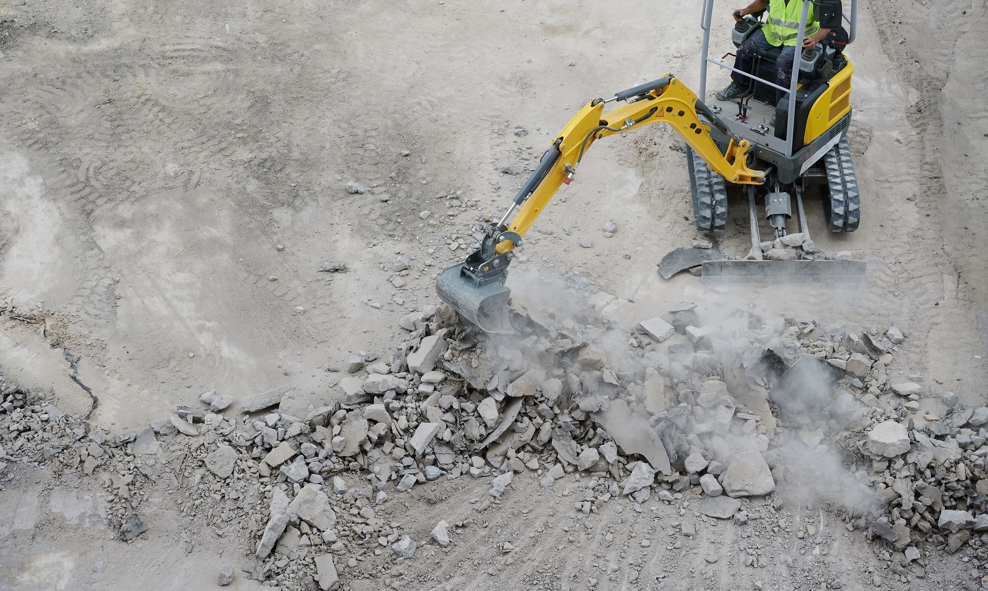 A man is driving a yellow excavator on a dirt road.