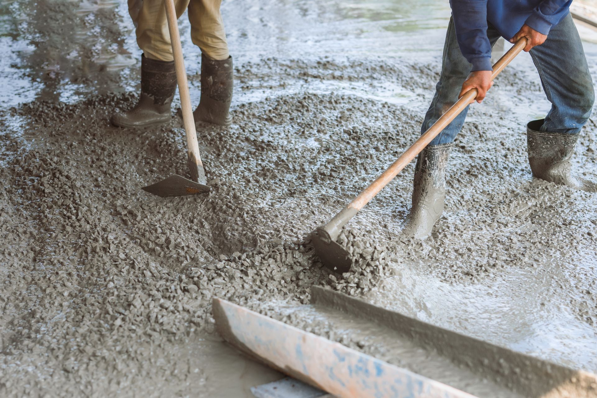 Two men are working on a concrete floor with shovels.