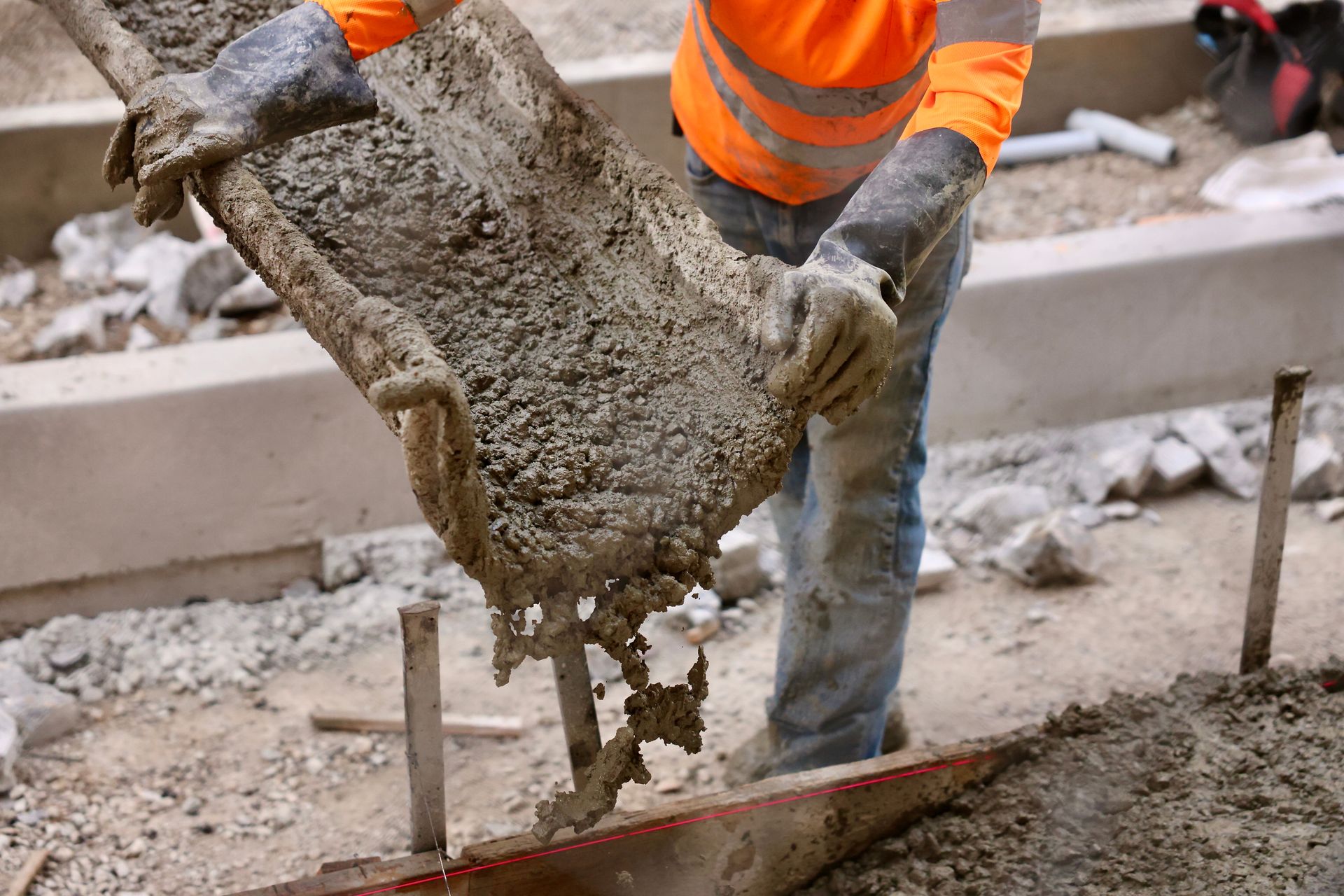 A construction worker is pouring concrete on a sidewalk.
