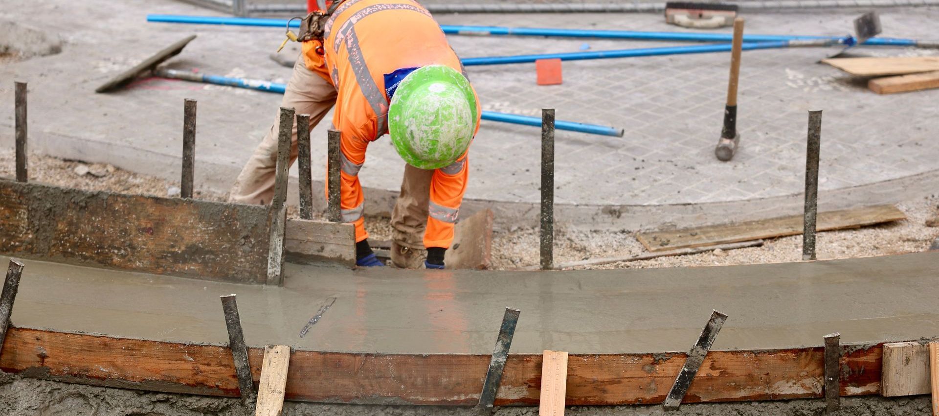 A construction worker is pouring concrete into a hole in the ground.