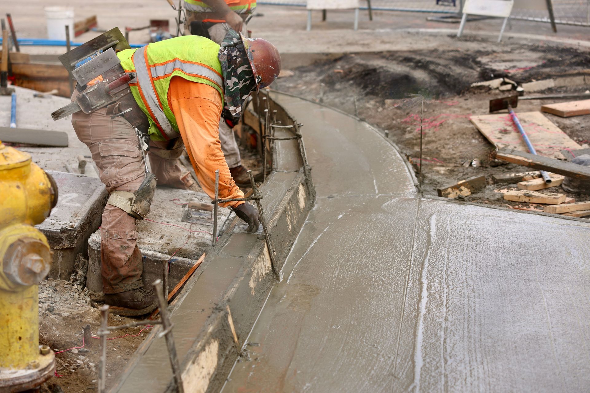 A construction worker is working on a sidewalk next to a fire hydrant.