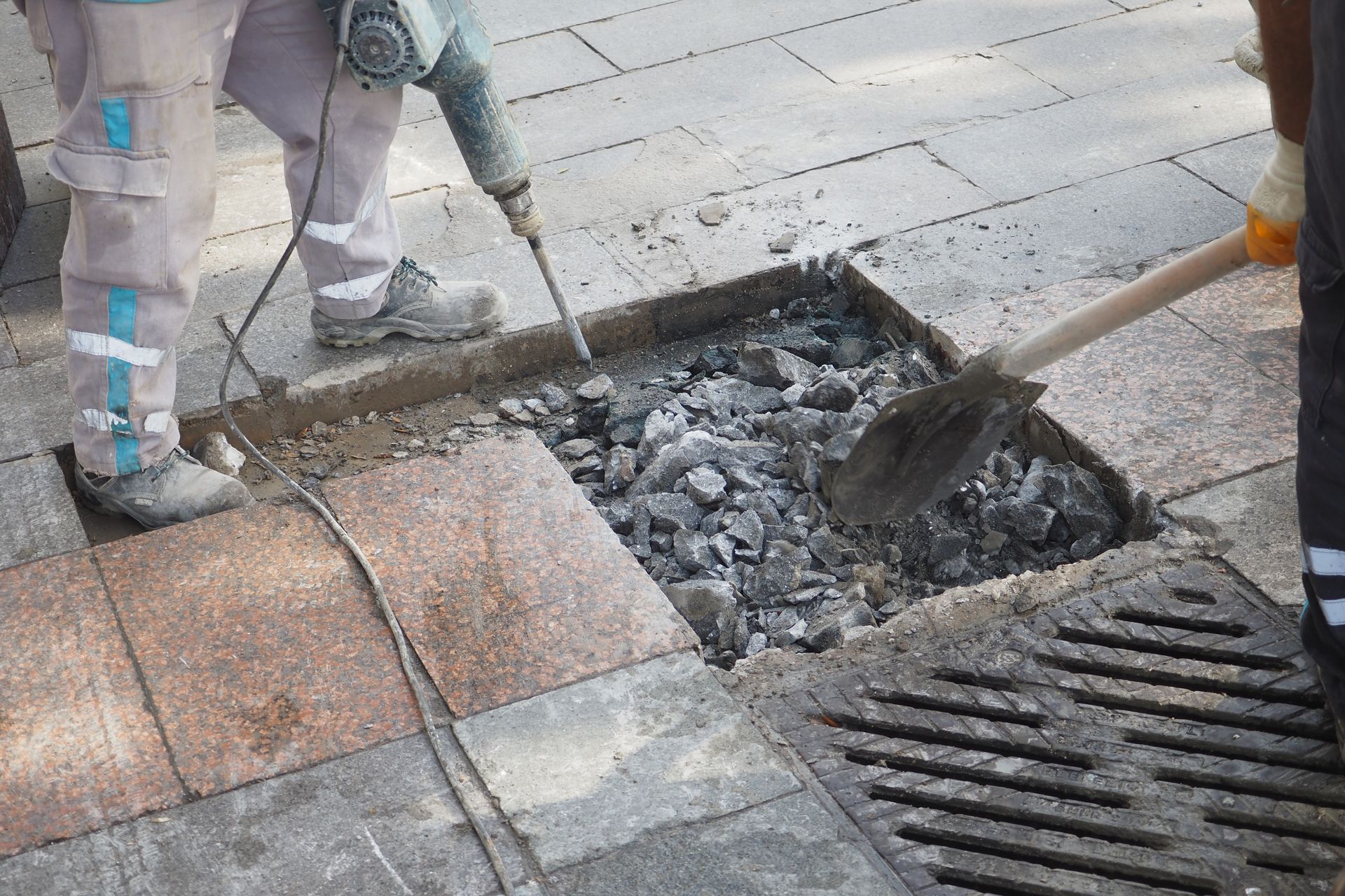 A man is using a hammer and a shovel to remove rocks from a hole in the ground.
