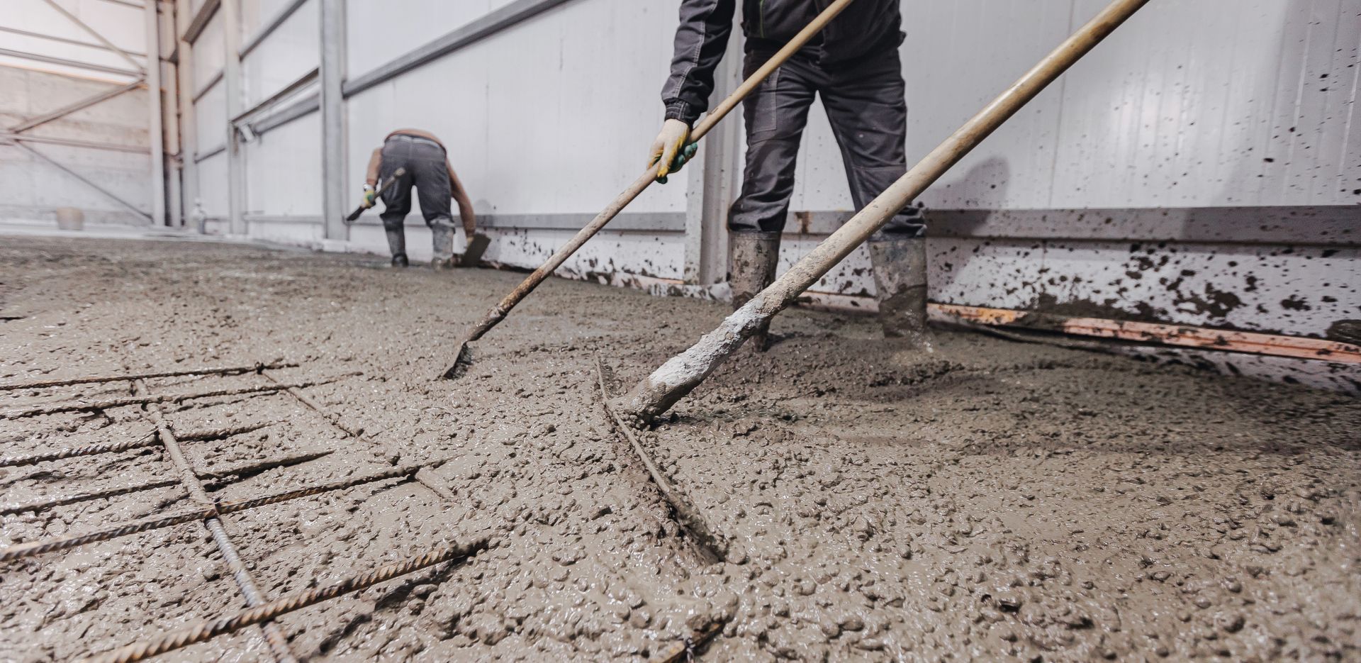 A man is raking a concrete floor with a rake.