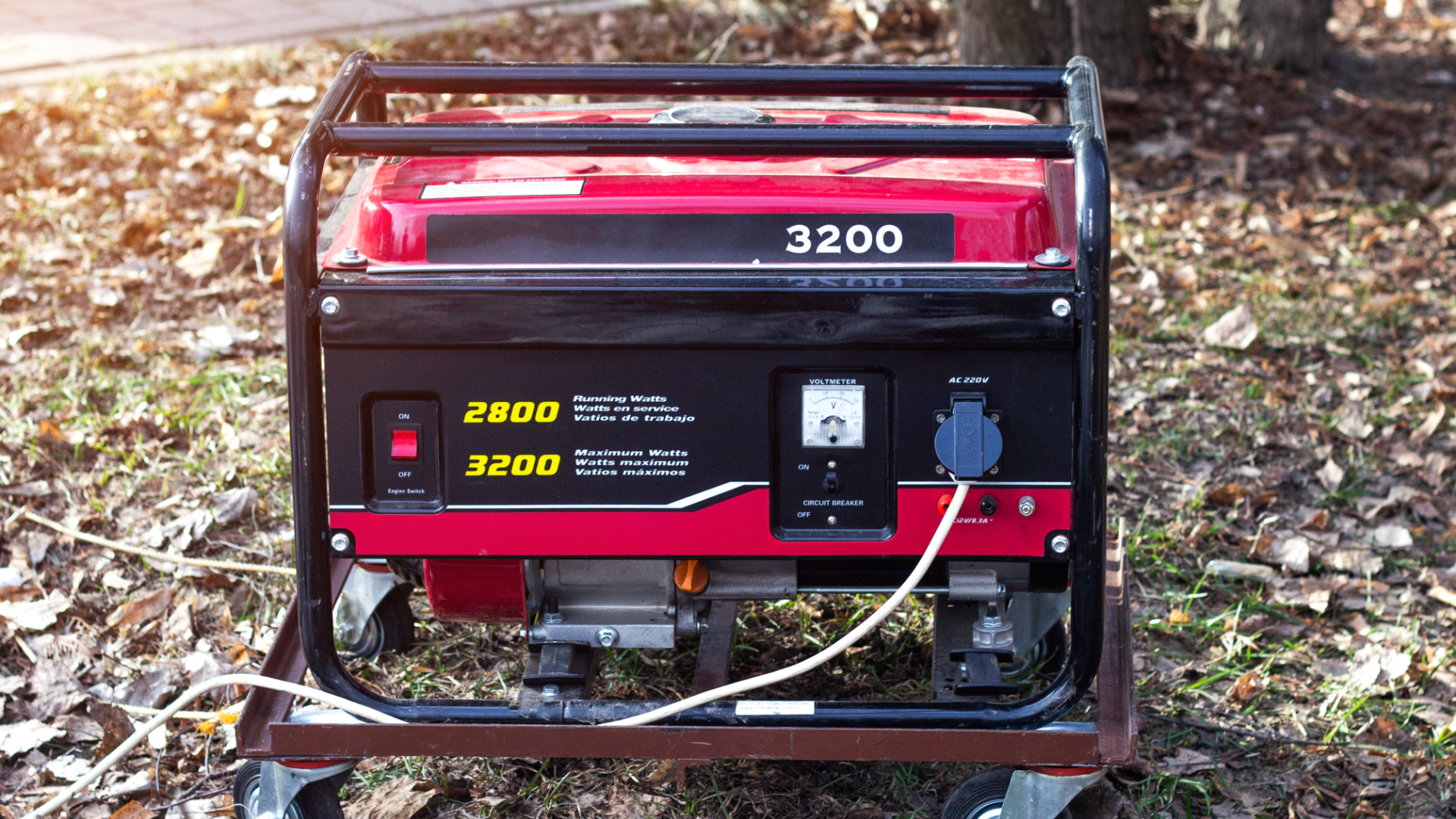 A red portable generator with black metal framing sitting on a metal platform amidst dry autumn leaves on the ground.