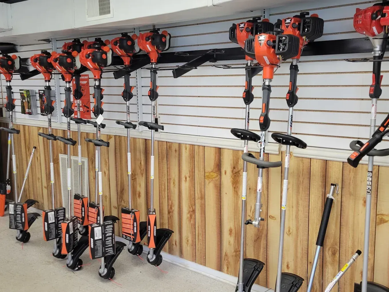 A row of orange string trimmers hangs on a wall rack in a retail store.