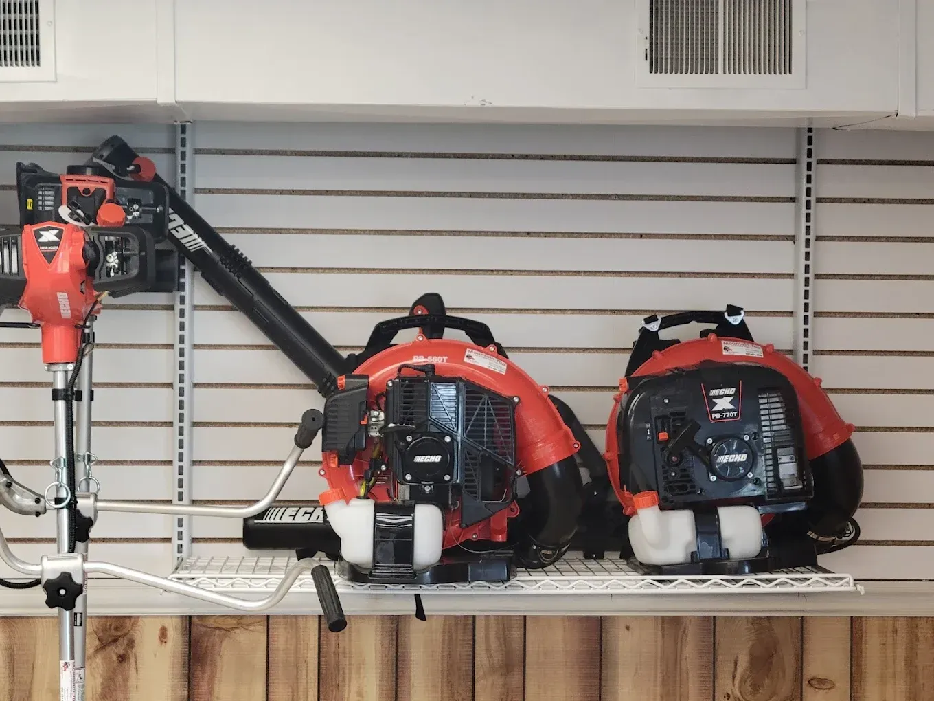 Three Echo brand leaf blowers on a display shelf against a slatwall, including a backpack style and a handheld model.
