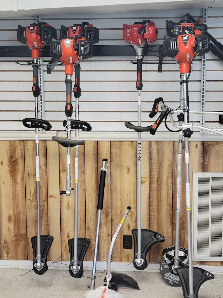 Several orange and black string trimmers hang on a display rack against a wood-paneled wall.