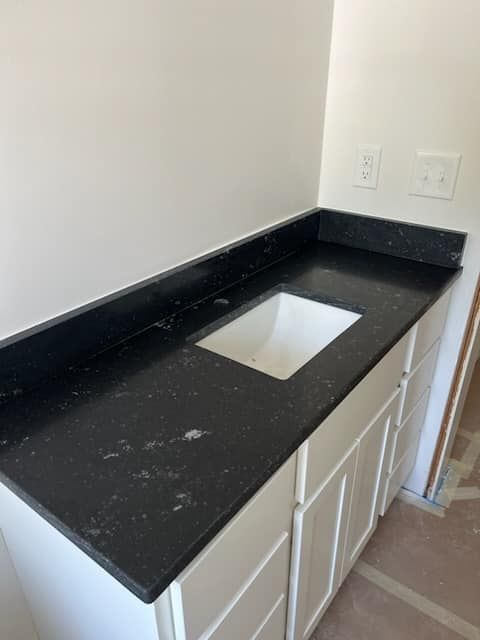 Black countertop with white sink and cabinets against a white wall.