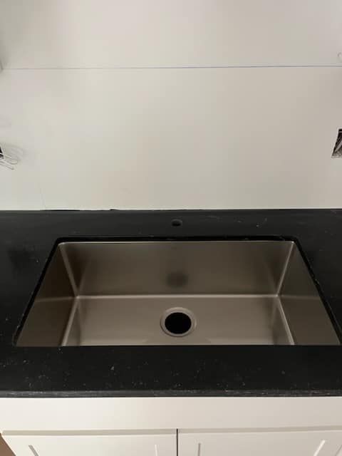 Stainless steel kitchen sink in black countertop.