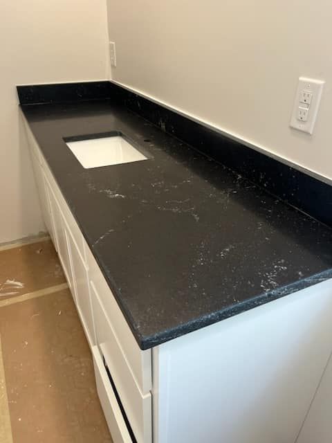 Black countertop on white vanity with rectangular sink.