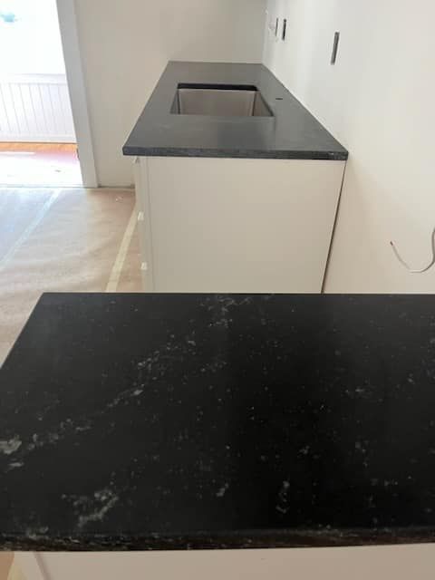Black countertops installed on white cabinets in a kitchen under construction.