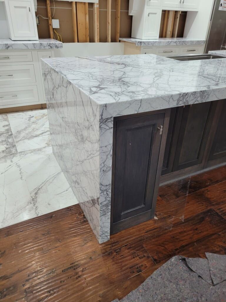 Marble-patterned countertop and cabinets in kitchen during renovation; wood floors and unfinished wall behind.