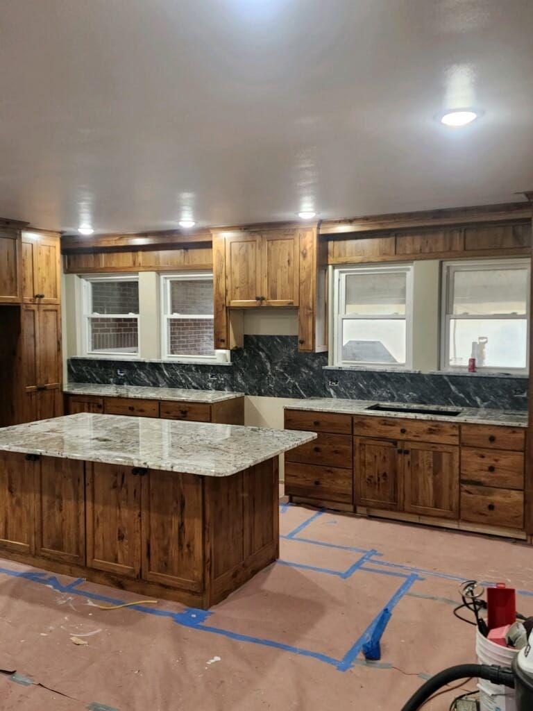 Wood-paneled kitchen with island and granite countertops, with windows and recessed lighting.