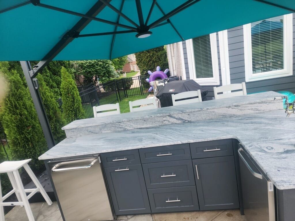 Outdoor kitchen with gray cabinets and granite countertop; blue umbrella overhead.