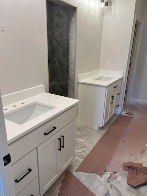 Two white bathroom vanities with black hardware; gray shower in background.