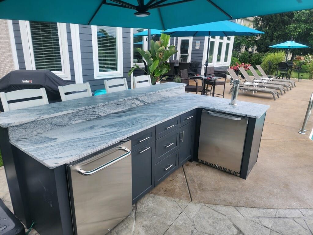 Outdoor kitchen with granite countertop, dark cabinets, stainless steel appliances, and umbrellas.
