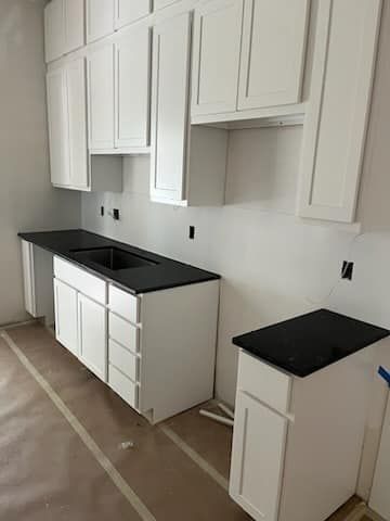 White kitchen cabinets with black countertops, under construction.