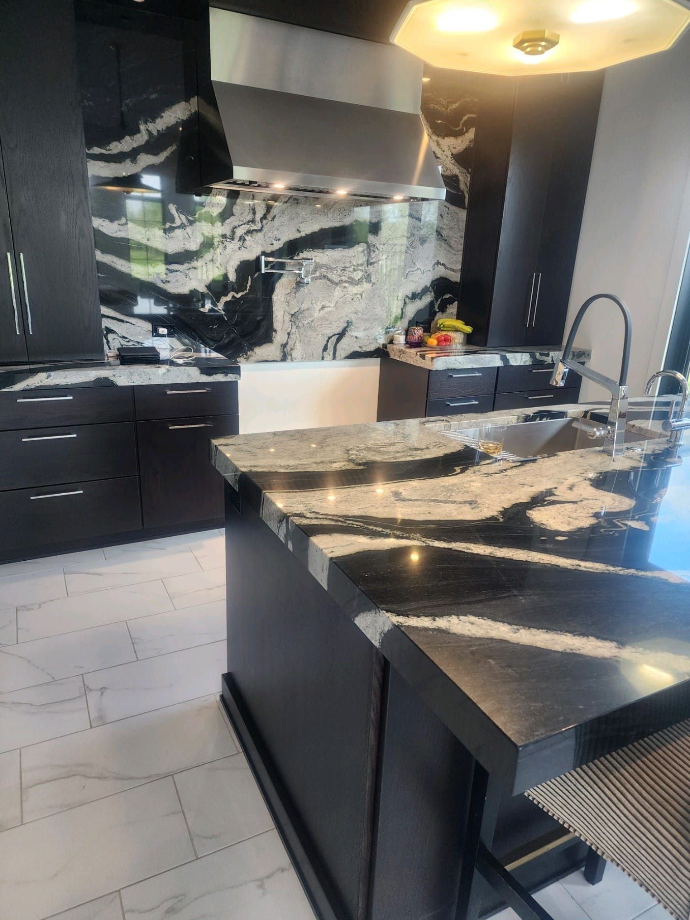 Modern kitchen with black cabinets, marble countertops, and stainless steel appliances.