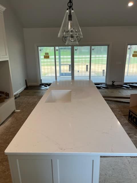 White kitchen island with sink, white cabinets, and modern light fixture.