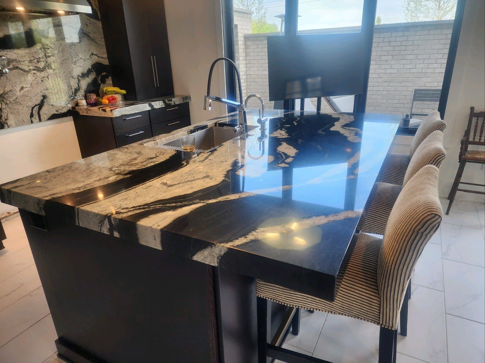 Kitchen island with black granite countertop, seating, and faucet. Dark cabinets and light tiled floor.
