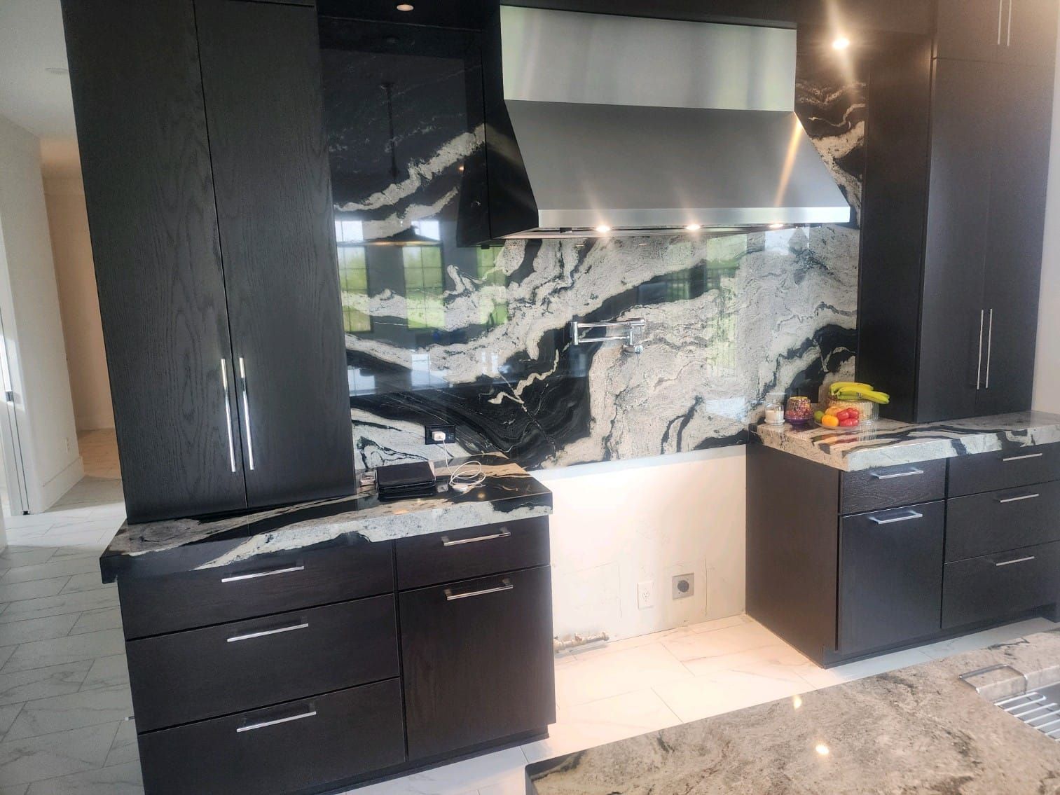 Black kitchen cabinets with granite countertop and backsplash. Stainless steel range hood.