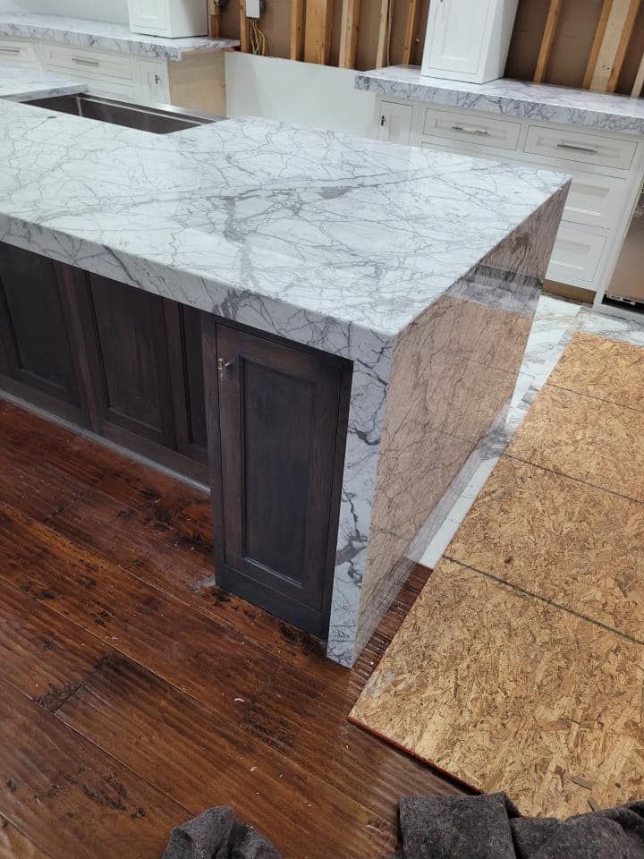 Kitchen island with marble countertop, dark cabinets, and hardwood floors. Construction in progress.