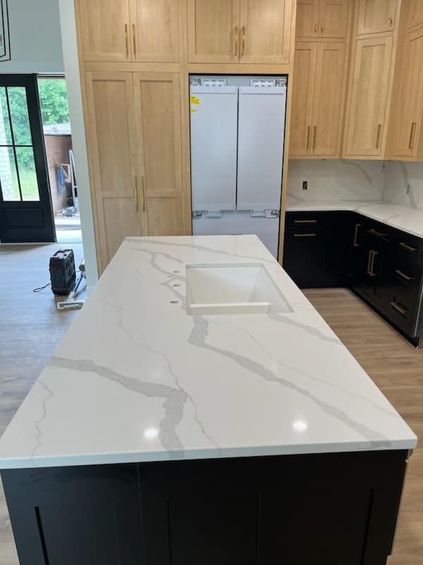Kitchen with white countertops, dark island, light wood cabinets, and stainless steel refrigerator.