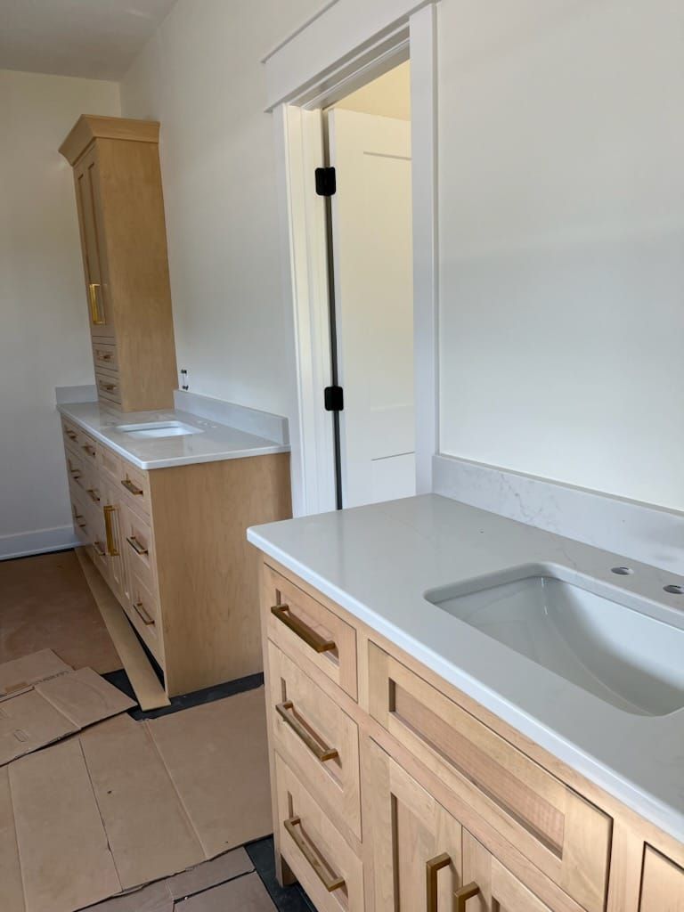 Light wood bathroom vanities with white countertops and a partially open doorway.