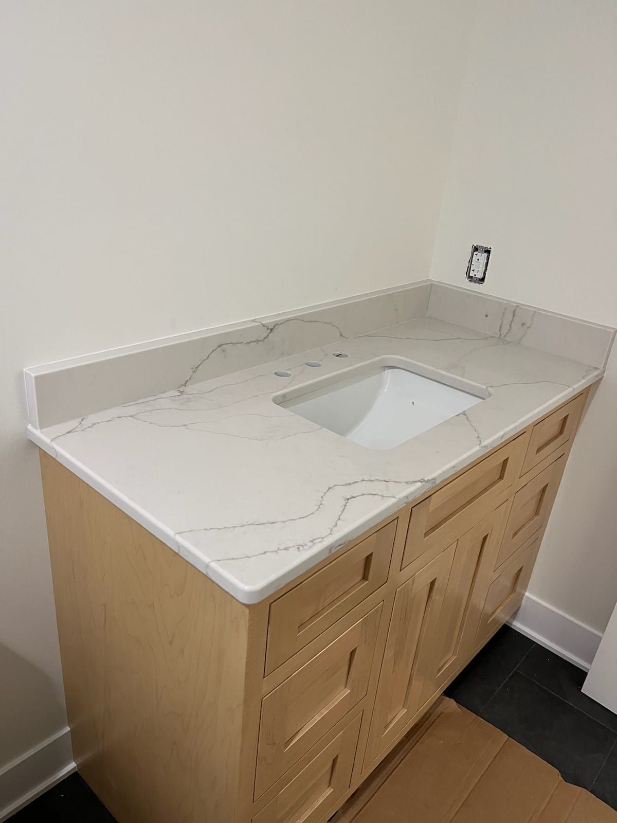 Bathroom vanity with white quartz countertop, light wood cabinet, and white sink.