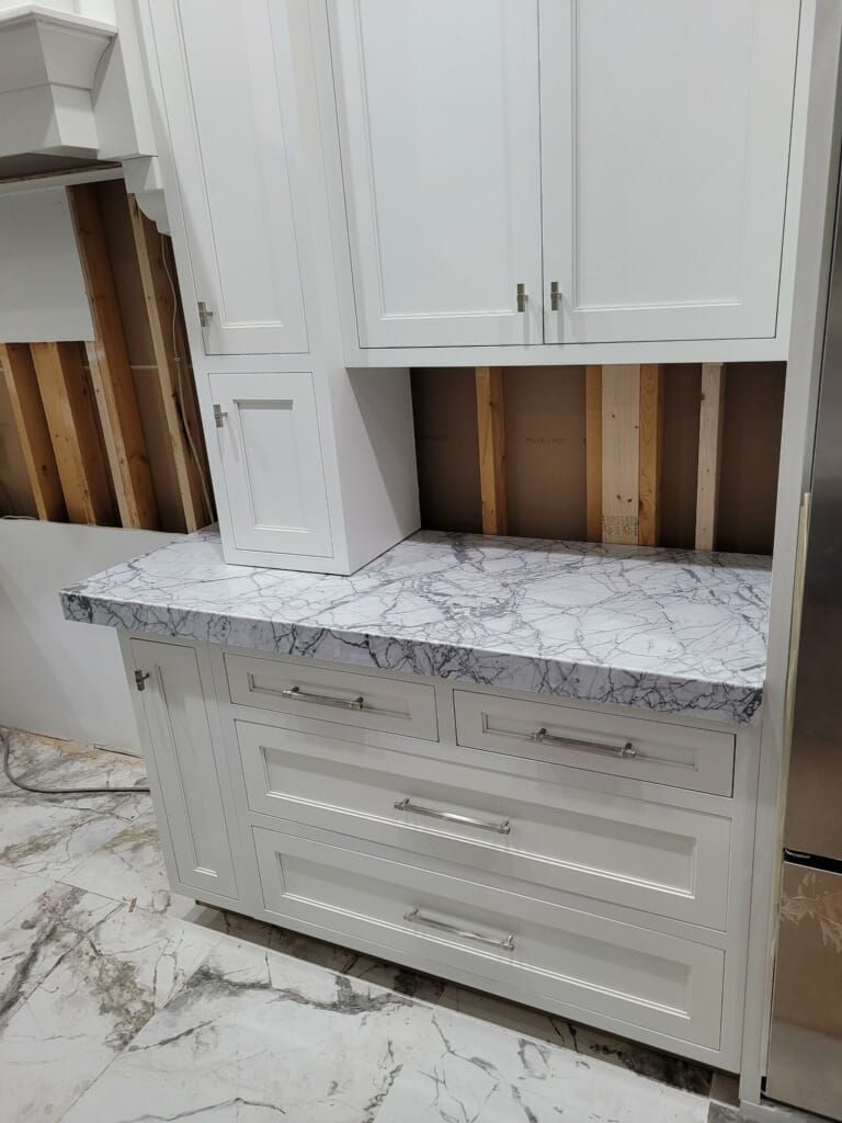 White kitchen cabinets with a marble countertop under construction.