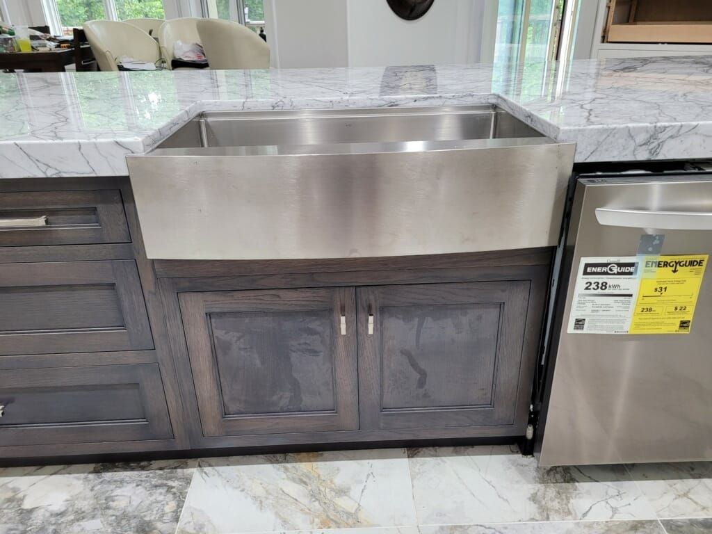 Stainless steel kitchen sink over gray cabinets, marble countertop.