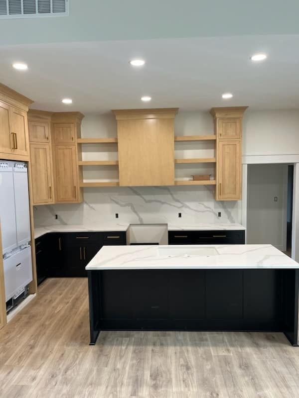 Modern kitchen with black island, light wood cabinets, and white countertops.