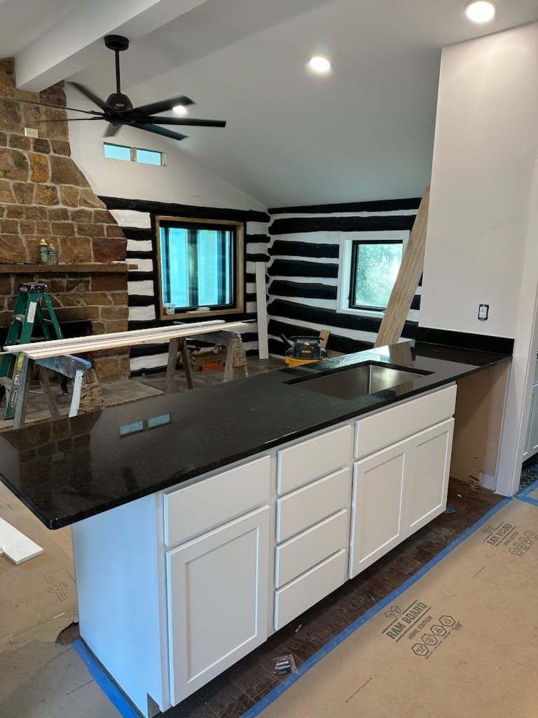 Kitchen with white cabinets, black countertop, black and white paneled walls, and a stone fireplace.