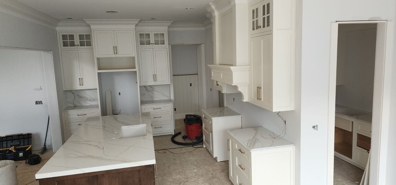 Kitchen with white cabinets, island, and countertops. Construction in progress.