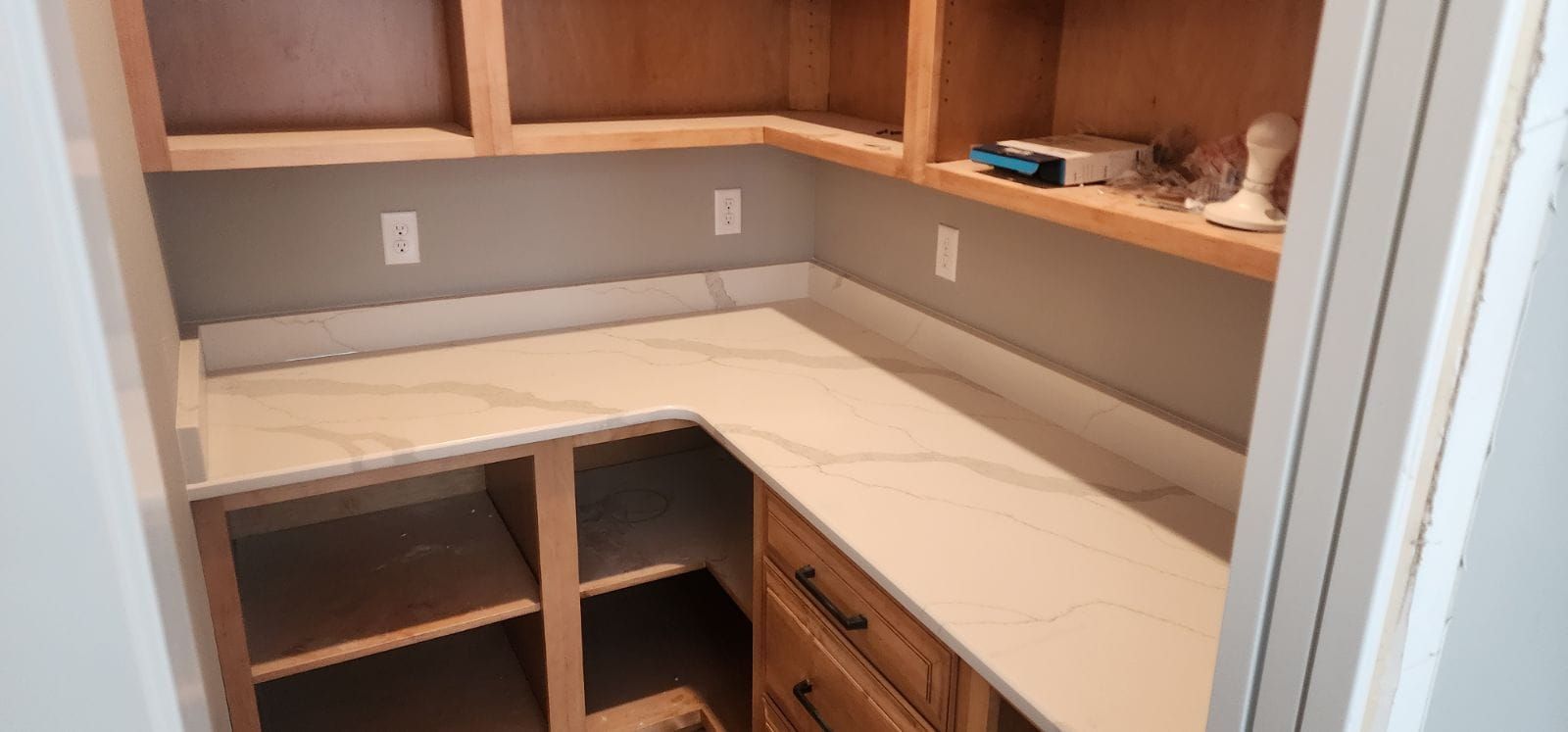 L-shaped pantry with white countertops, unfinished cabinets, and a neutral-toned wall.
