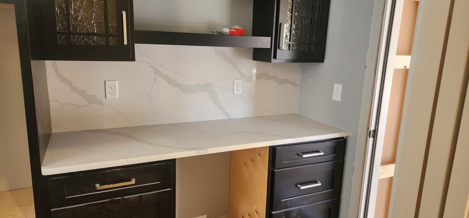 Built-in desk with cabinets; black cabinets and white countertop and backsplash.