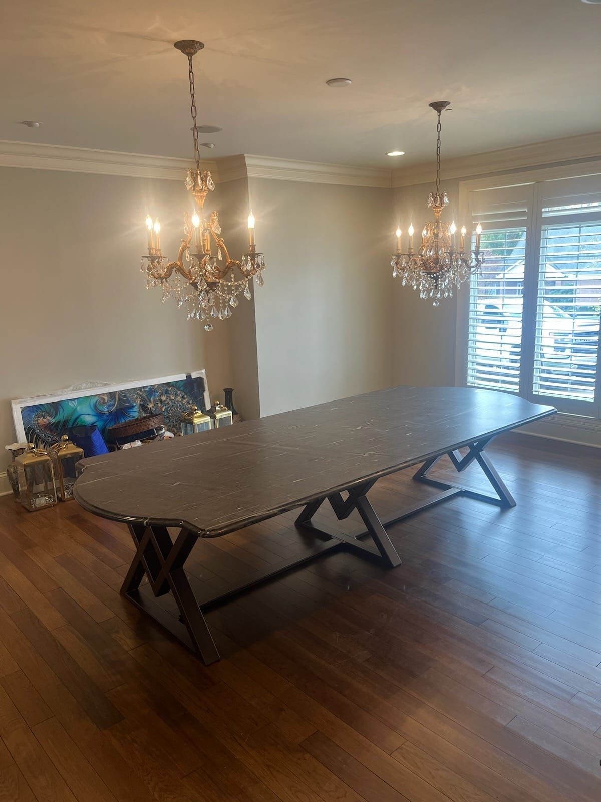 Long dining table with metal legs, chandeliers, wood floor, and large windows.