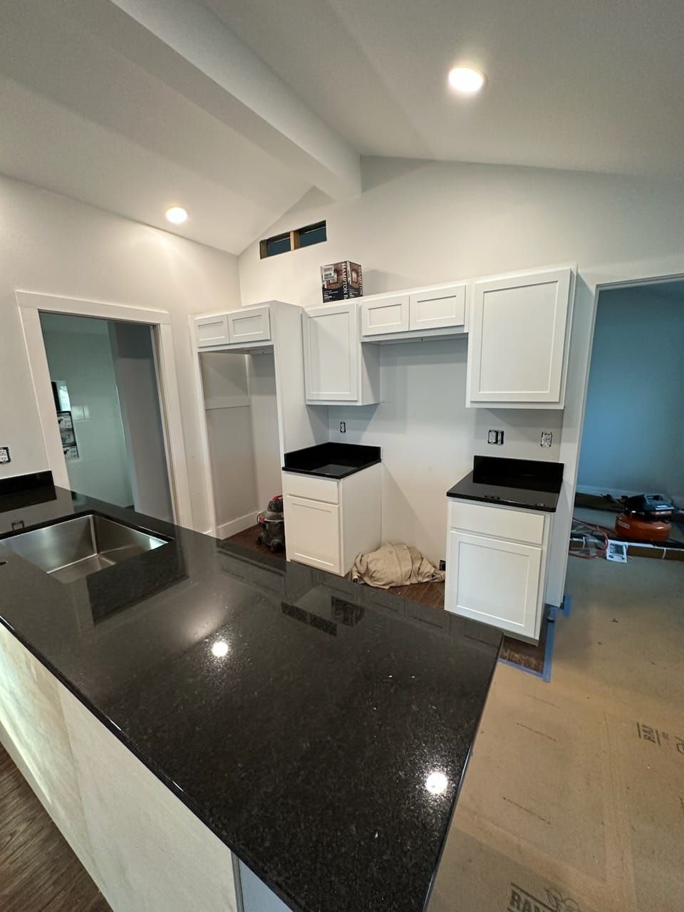 Kitchen under construction with white cabinets, black countertops, and an island.