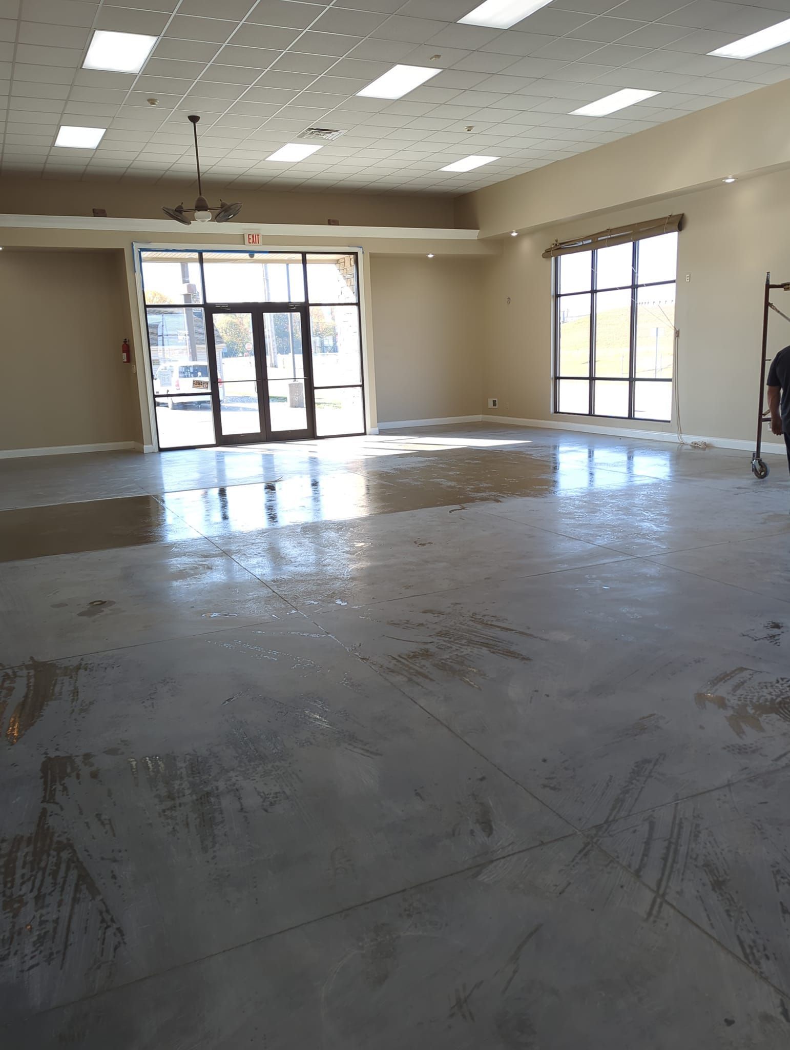 Empty, large room with a wet, reflective floor. Beige walls, windows, and door.