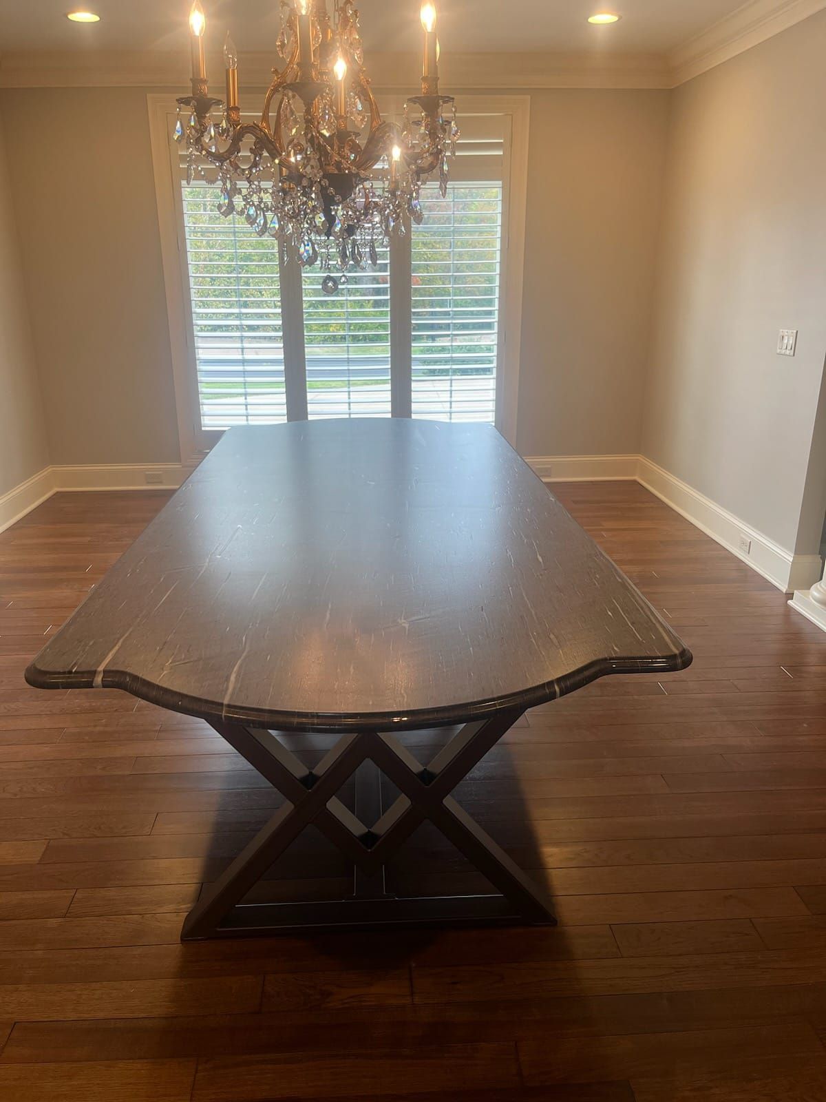 Dining room with a large rectangular dark wood table, ornate chandelier, and window with shutters.