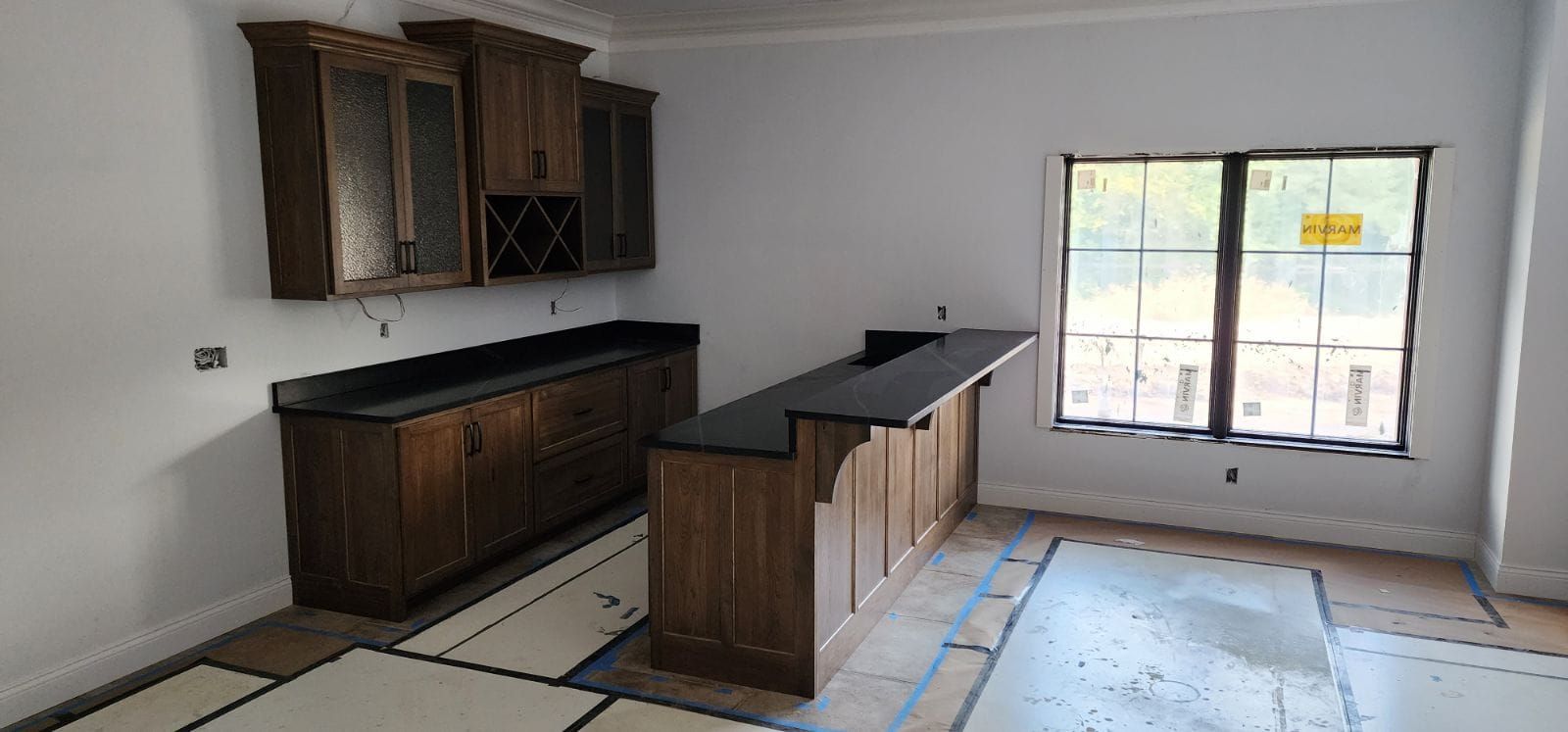 A wooden bar with dark countertops and cabinets against a white wall, near a window.