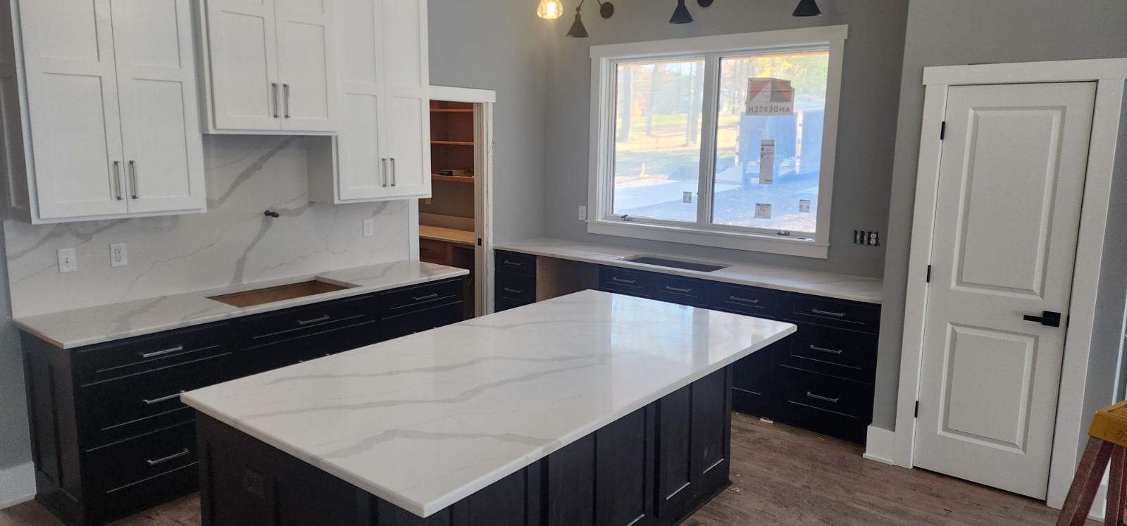 Kitchen with black cabinets, white countertops, and an island. White upper cabinets and a window.