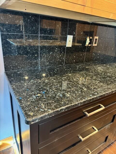 Dark granite countertop and backsplash with dark brown cabinets, gold hardware.