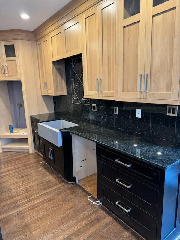 Kitchen with light wood upper cabinets, black lower cabinets, and black countertops; stainless steel sink.
