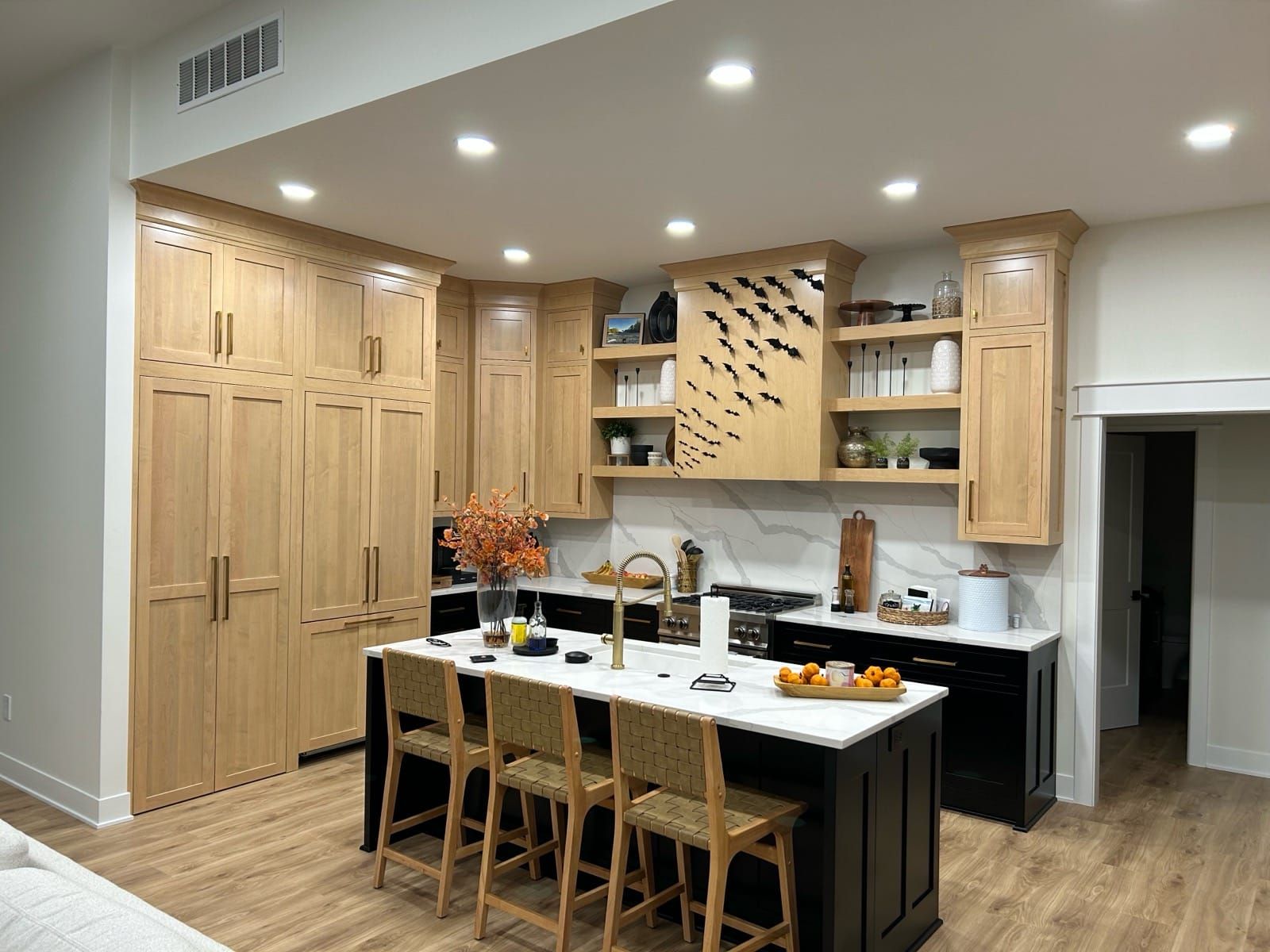Modern kitchen with light wood cabinets, black island, and marble countertops; brown wood flooring.