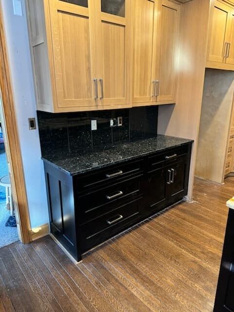 Kitchen cabinets: light wood uppers, black lower cabinets and countertop, hardwood floor.