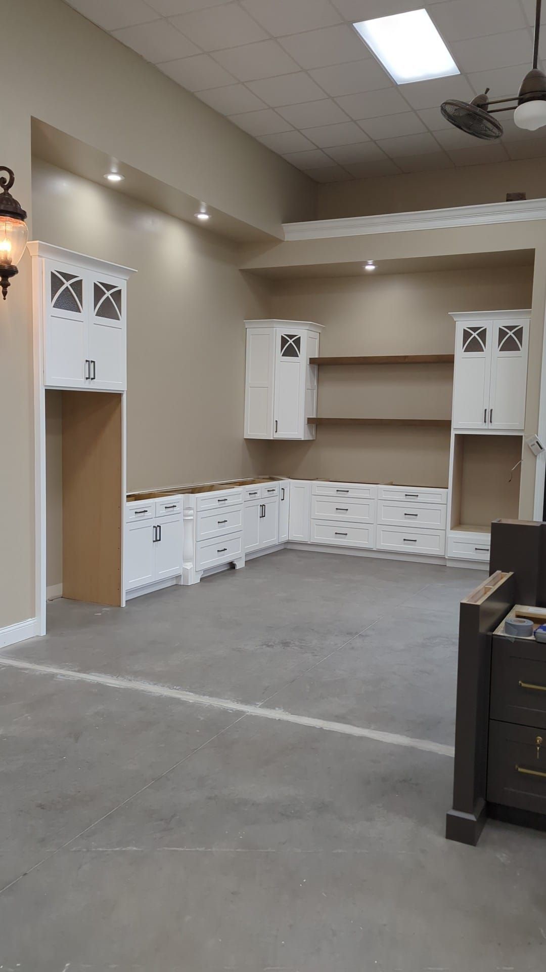 New kitchen under construction; white cabinets, neutral walls, concrete floor, recessed lighting.