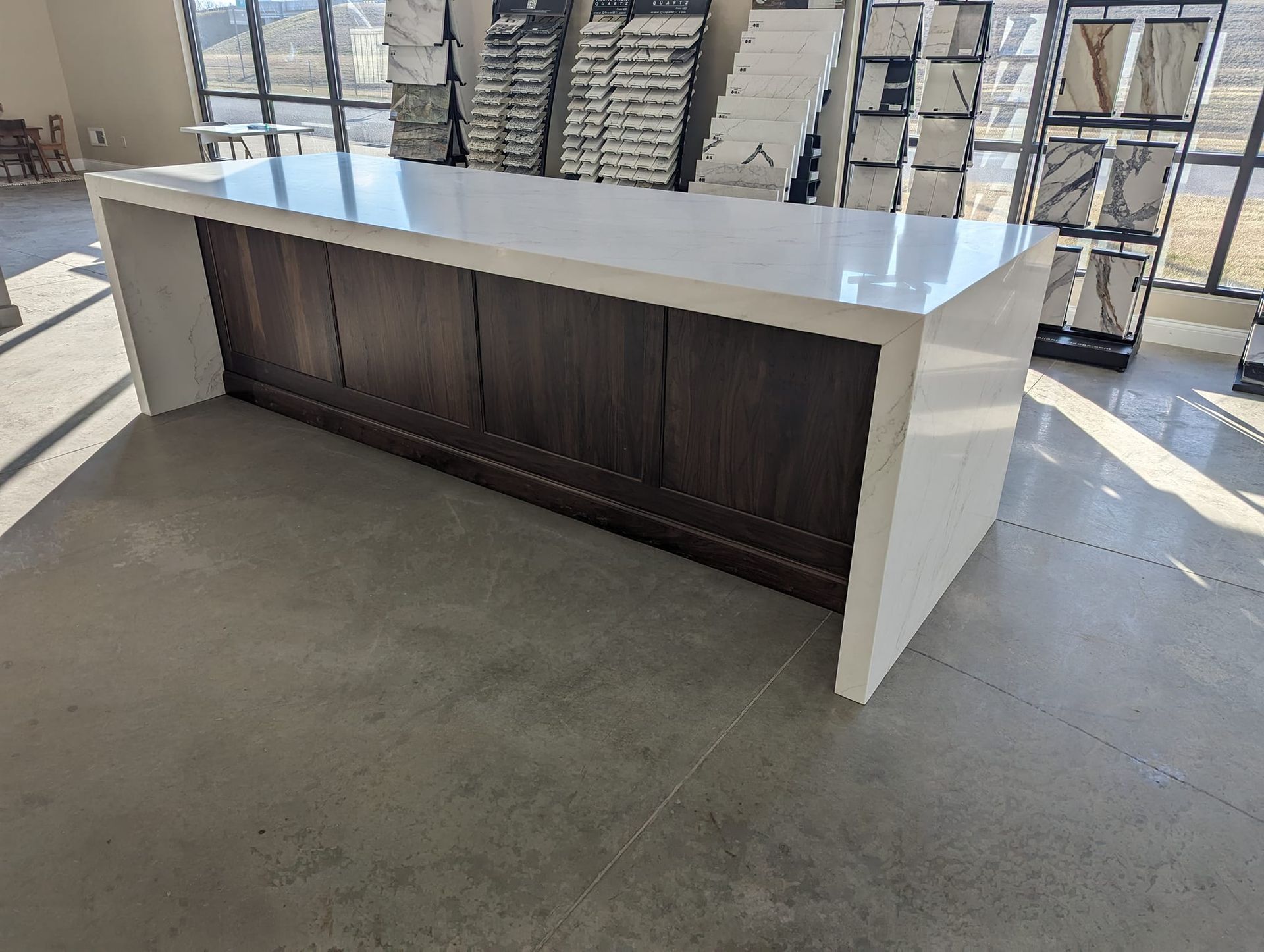 A large kitchen island with white countertop, dark wood cabinets, and concrete floor.