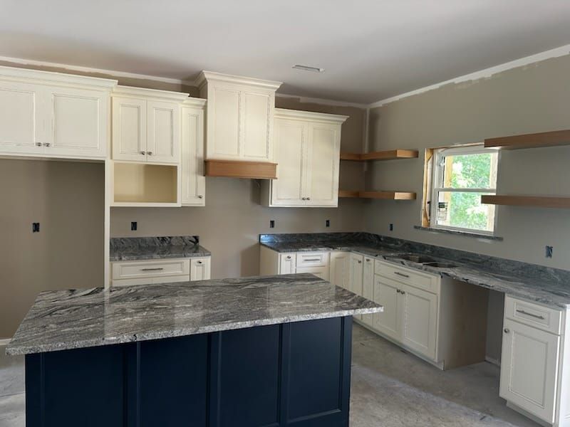 Kitchen with white cabinets, blue island, granite countertops, and floating shelves.