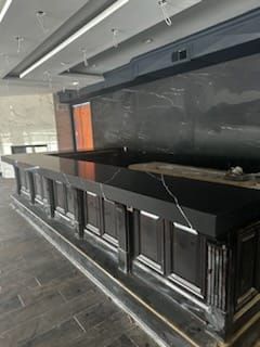 A dark, newly-built bar with black marble countertop, dark wood paneling, and a black marble backdrop.